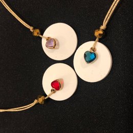 Courassoun lucky charm keychains in rouge, bleu, and rose colors, featuring round discs with colorful gemstones.