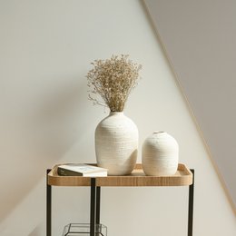 Tall, cylindrical white ceramic vase with textured surface. Displayed on a wooden shelf with a smaller vase and glass bottle.