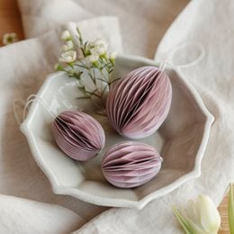Paper Easter eggs in soft pink color, arranged on a white plate with lily of the valley flowers.