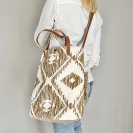 Beige bucket bag with Aztec-inspired pattern, worn with a tan cardigan, denim shorts, and strappy sandals.