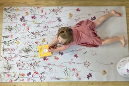 Large floral pattern playmat with a young girl lying on it, surrounded by various colorful flowers and plants.
