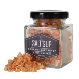 Chili crystal salt flakes in a glass jar. The salt flakes have an orange-red color and appear to be coarse in texture.