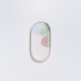 Oval-shaped white ceramic jewelry tray with pastel-colored abstract shapes.