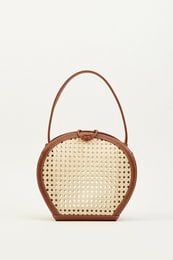 Brown woven handbag with round shape and leather trim.