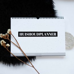 A white spiral-bound planner with the text "HOUSEHOLD PLANNER" printed on the cover, surrounded by dried flowers and twigs against a dark background.
