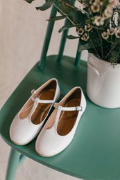  White leather ballet flats with strap detail, suitable for girls' First Communion or other formal occasions. Features a classic, simple design in a versatile color.