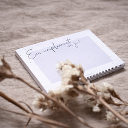 A white notepad with the handwritten text "En compliment pour vous!" (French for "A compliment for you!") surrounded by dried flowers.