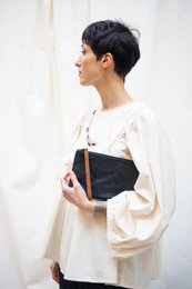 Black leather clutch with a minimalist design and a tan leather strap.