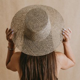 A wide-brimmed, woven straw hat with a natural, textured appearance. The hat features an open, airy design and is suitable for summer wear.
