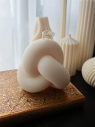 Ribbed, knot-shaped pillar candle in a neutral, off-white color.