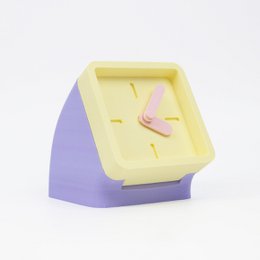 A small, square table clock with a yellow and purple color scheme. The clock face features a pink clock hand.