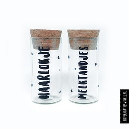 Two glass jars with cork lids labeled "Lock of hair" and "Milk teeth" for storing keepsakes.