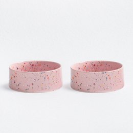  Two round, speckled pet food bowls in pink color. The bowls appear to be made of ceramic or a similar material.