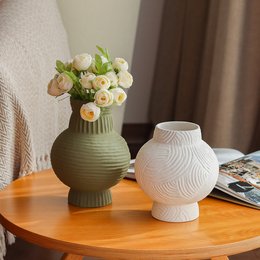 A decorative vase with a bouquet of white and yellow flowers, and a second vase on a wooden table.

The image shows a green ceramic vase filled with a bouquet of white and yellow flowers, likely roses or peonies. The vase has a textured, ribbed design. Next to it is a second white ceramic vase with a smooth, minimalist design. Both vases are placed on a wooden table or surface.