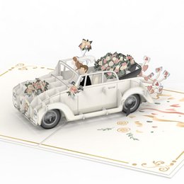 A pop-up wedding card featuring a vintage-style car carrying a bride and groom, surrounded by flowers and decorative elements.