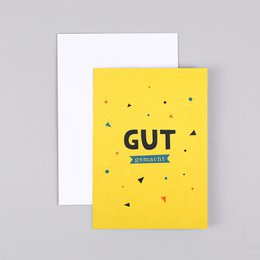 Folding card with the text "Gut" printed in a bold, stylized font against a yellow background. The card is accompanied by a blue envelope, suggesting it is a greeting card or invitation.