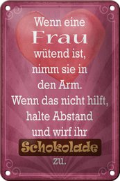 A decorative tin sign with a humorous German text about a woman's anger and the solution of chocolate. The sign features a pink background with a vintage-style design.