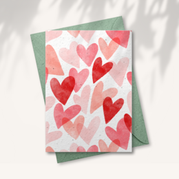 A heart-patterned greeting card in a terracotta plant pot with the text "Seeds inside!" This love-themed card features a vibrant red heart pattern and is presented in a rustic terracotta pot, suggesting it may contain seeds or other small items inside.