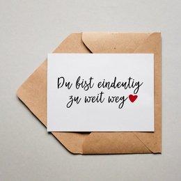 A romantic greeting card with a handwritten message in German that translates to "You are definitely too far away." The card is placed on a brown envelope against a light background.