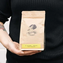 Whole bean coffee from El Salvador, Lombardia region, with an espresso roast profile. Packaged in a beige paper bag with a logo.