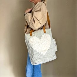 Beige canvas tote bag with a large white heart-shaped applique, suitable for carrying as a shoulder bag.