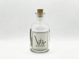 100ML clear glass diffuser bottle with various fragrance names on the label, including Sapin Magique, Joie de Noël, Douceur Coton, and others. The bottle has a cork stopper and is accompanied by a cardboard box.