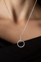 A delicate, circular pendant necklace made of silver-toned metal with a simple, minimalist design.