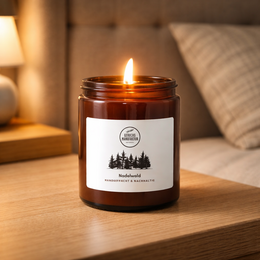A tall, round, amber-colored glass candle jar with a pine forest design label. The candle is scented with a "Nadelwald" or pine forest fragrance.