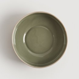 A round, shallow ceramic bowl in a muted green color. The bowl has a simple, minimalist design with a smooth, glazed surface.
