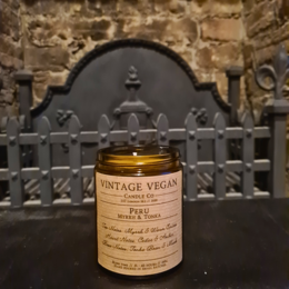 Vintage vegan soy wax candle with Peru myrrh and tonka scent, featuring an ornate metal lid and decorative stone wall backdrop.