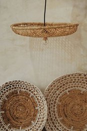 A woven, round lamp shade made of natural materials, likely rattan or wicker. The lamp shade has a simple, rustic design with a hanging cord.