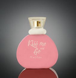  A pink, heart-shaped perfume bottle with the text "Kiss me and go" printed on it. The bottle has a white cap and a gold-colored accent.