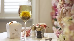 A glass of tea with a yellow flower, a package, and a woman holding a glass of wine in a garden setting.