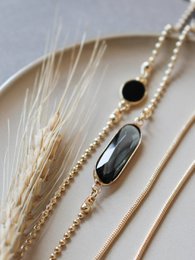  Gold-toned necklace with elongated black stones and delicate chain details.