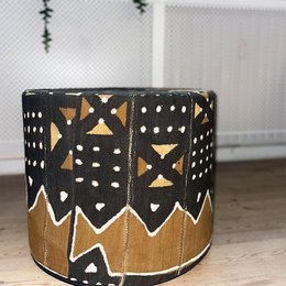A round, wooden stool with a black and tan geometric pattern, suitable for use as an ottoman or footstool.
