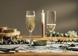 Elegant champagne glasses with a plissé design, holding 210ml of champagne. The glasses are arranged on a table with a candle and other decorative elements, creating a sophisticated and festive atmosphere.