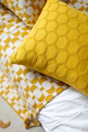 A soft, yellow cotton knit pillow cover with a textured hexagon pattern, suitable for use as a decorative cushion on a couch or chair.