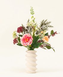  Vibrant bouquet of pink roses, greenery, and other colorful flowers in a white ceramic vase.