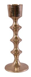  A tall, cylindrical candle holder made of shiny metallic material, likely copper or bronze in color. The candle holder has a simple, elegant design with a smooth, reflective surface.