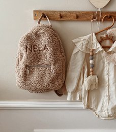 Beige children's backpack with embroidered "NELA" text and plush, fuzzy material.