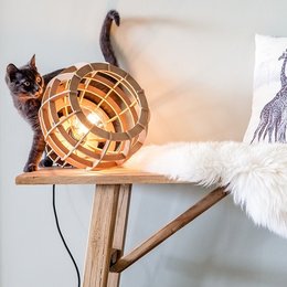 A natural-colored, globe-shaped table lamp with a wooden frame and a black cat sitting on top of it.