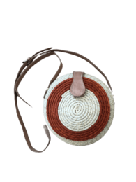 A round, woven crossbody bag in shades of brown and white with a leather strap.