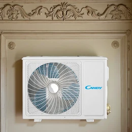  A white air conditioning unit with the Candy brand name, mounted on a wall above a fireplace. The air conditioning unit has a circular fan design and appears to be a high-efficiency model.