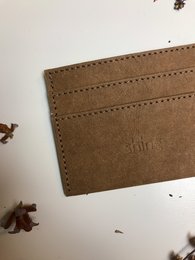 Camel-colored leather card holder with stitched edges and a minimalist design.