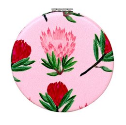 Compact two-sided mirror with a pink background and vibrant red and green protea flowers. Ideal for makeup application and touch-ups on the go.