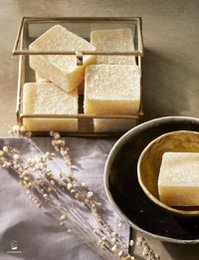 Vanilla-scented amber-colored soap blocks, packaged in a clear display case, with a sprig of lavender visible.