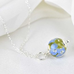 Delicate necklace with periwinkle glass flowers and a miniature globe charm. Elegant and nature-inspired design.