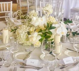 Tall, round white pillar candle with a floral arrangement of white flowers and greenery.