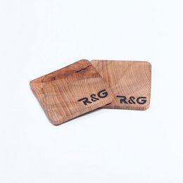 Two wooden coasters with "R&G" printed on them. The coasters have a natural wood grain texture and appear to be made of a durable material.