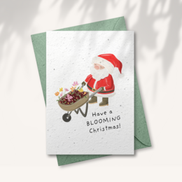 Seed paper Christmas card with a Santa Claus figure pushing a wheelbarrow full of blooming flowers, conveying a "have a blooming Christmas" message.